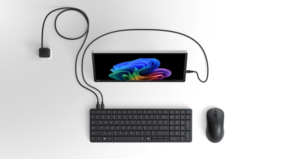 The HP EliteBoard G1a keyboard connected to a single monitor by one braided cable, alongside a wireless mouse and a compact power adaptor - a complete PC with no tower and no cable clutter.