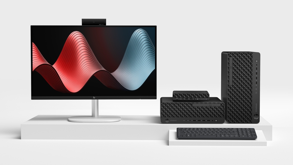 The HP EliteBoard G1a - a slim keyboard-sized unit - shown beside a traditional small-form-factor desktop and a full tower, illustrating how much desk space the keyboard PC saves.