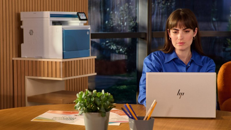 A professional at an HP laptop with an HP multifunction printer in a modern office